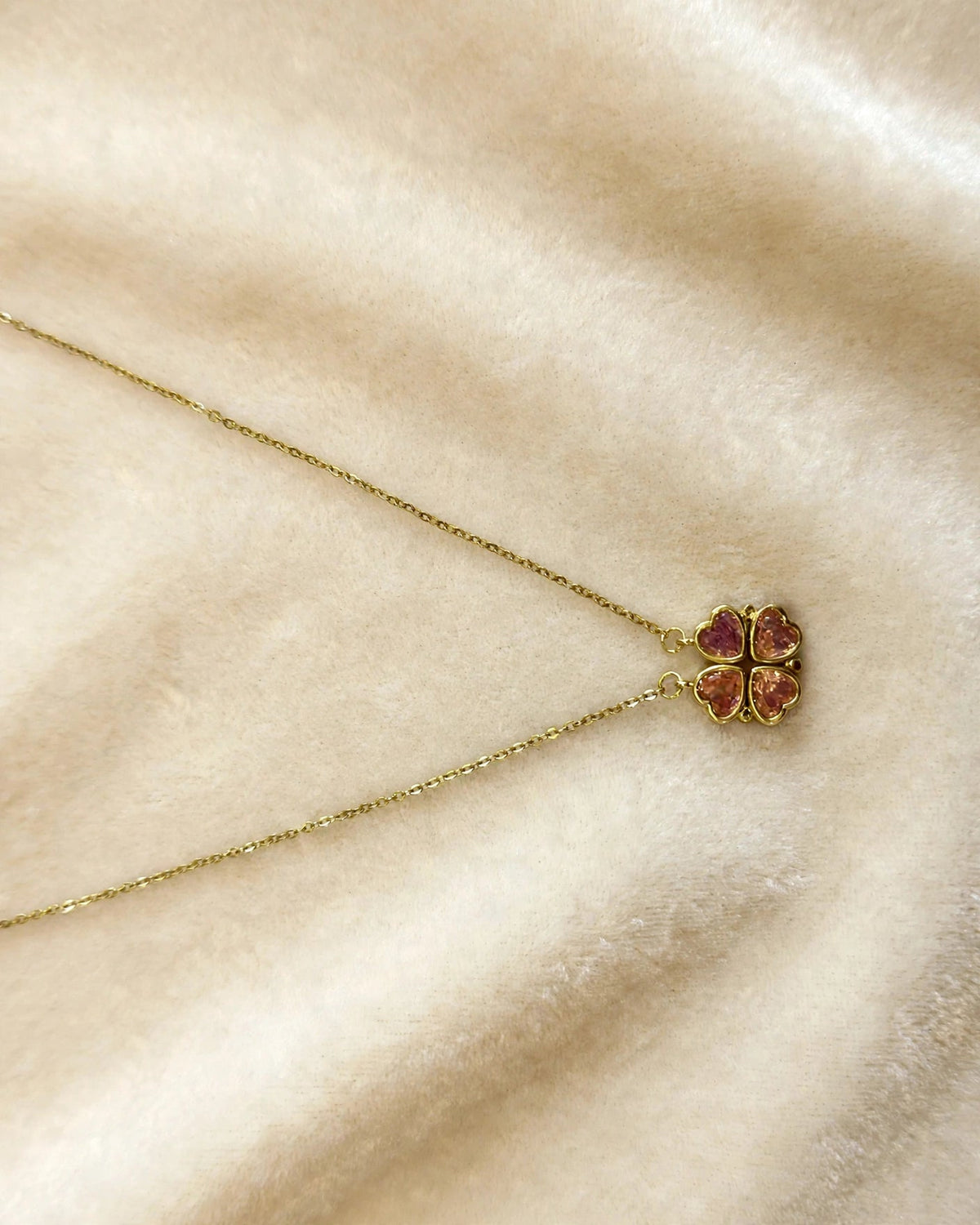 Gouden klavertje-vier ketting met roze zirkonia hartjes op crème achtergrond